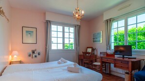 A bedroom with two beds, a desk, a television, and large windows.