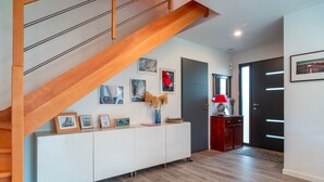 A modern interior with a wooden staircase, a white console table with framed pictures, and a red lamp. - Ti Marsouin - Jolie maison avec extérieur (La Trinite-sur-Mer)