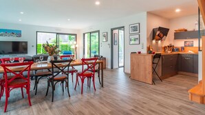 A modern kitchen with wooden cabinets, a dining area with red chairs, and a large window offering a view of greenery. - Ti Marsouin - Jolie maison avec extérieur (La Trinite-sur-Mer)