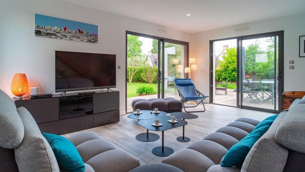 A modern living room with a flat-screen TV, a sofa, a coffee table, and a chair. There is a sliding glass door leading to an outdoor patio area. - Ti Marsouin - Jolie maison avec extérieur (La Trinite-sur-Mer)