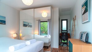 A hotel room with a bed, a desk, a chair, a mirror, and a window with curtains. - Ti Marsouin - Jolie maison avec extérieur (La Trinite-sur-Mer)