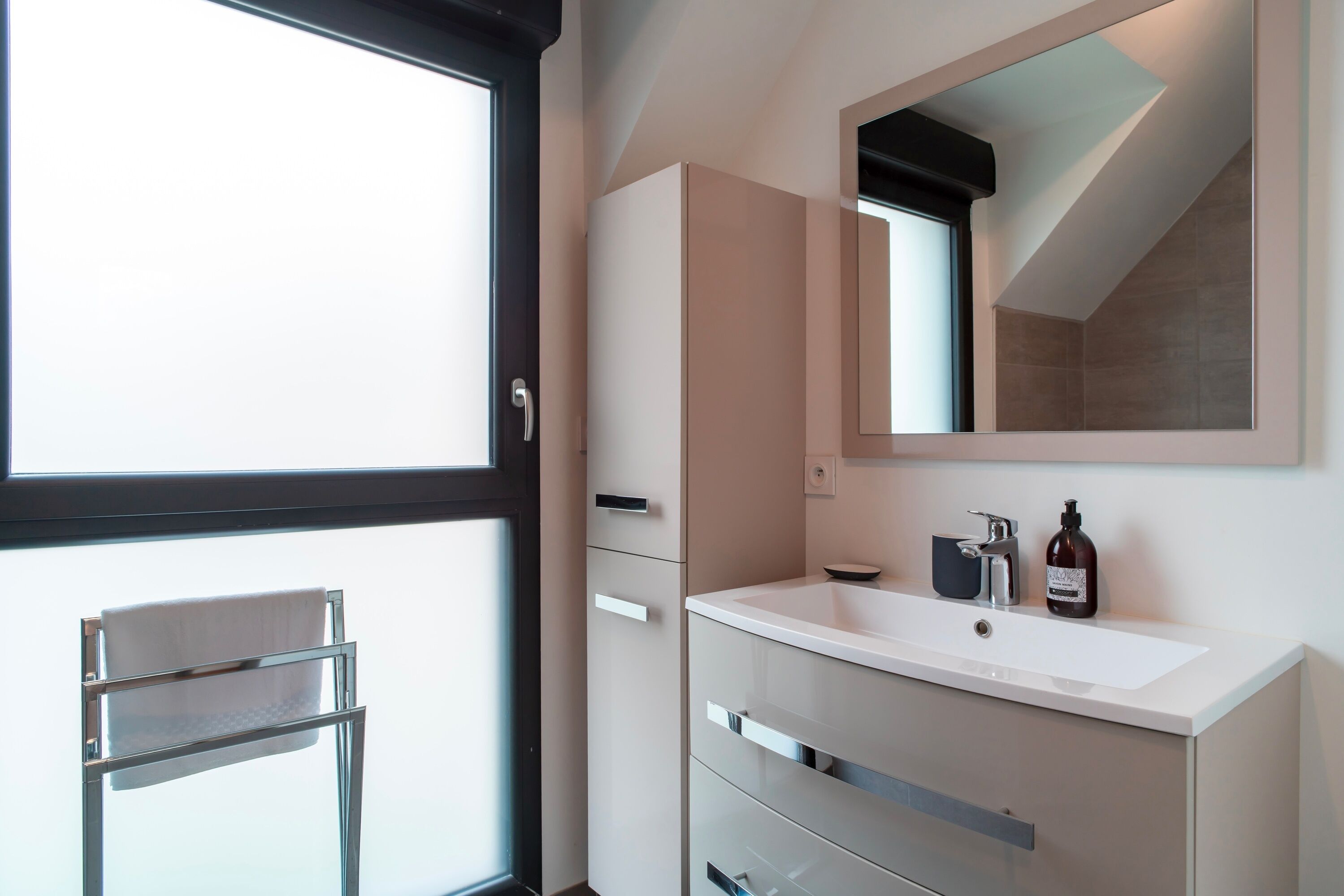 Une salle de bain moderne avec une grande fenêtre, un lavabo blanc, un miroir et un porte-serviettes.