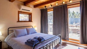 Une chambre à coucher avec un lit, une fenêtre, des rideaux, un appareil de climatisation et un plafond en bois.