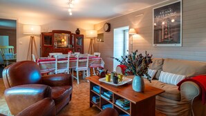 Una sala de estar acogedora con un sofá de cuero marrón, una mesa de centro de madera con libros, una mesa de comedor con mantel a rayas rojas y blancas y un póster en la pared.