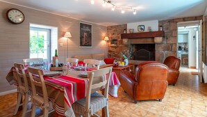 Un comedor con mantel rojo, sillas de madera, chimenea de piedra y un reloj en la pared.
