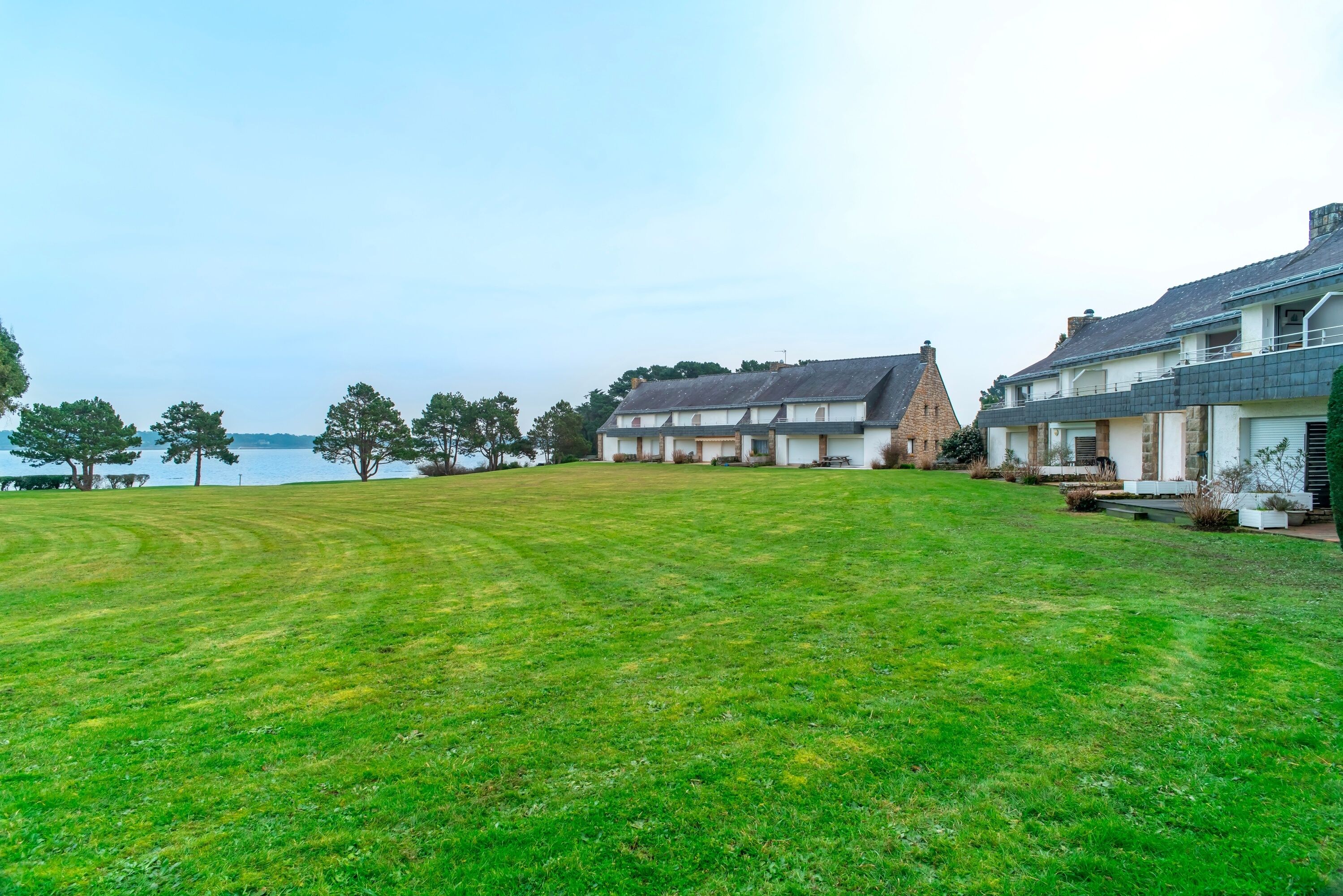 A large, open grassy area with a view of a lake and two buildings with a modern design.