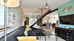 Ein modernes Wohnzimmer mit schwarzem Sofa, einem Couchtisch, einem Fernseher auf einem schwarzen Schrank und einer Treppe, die in einen anderen Raum führt.