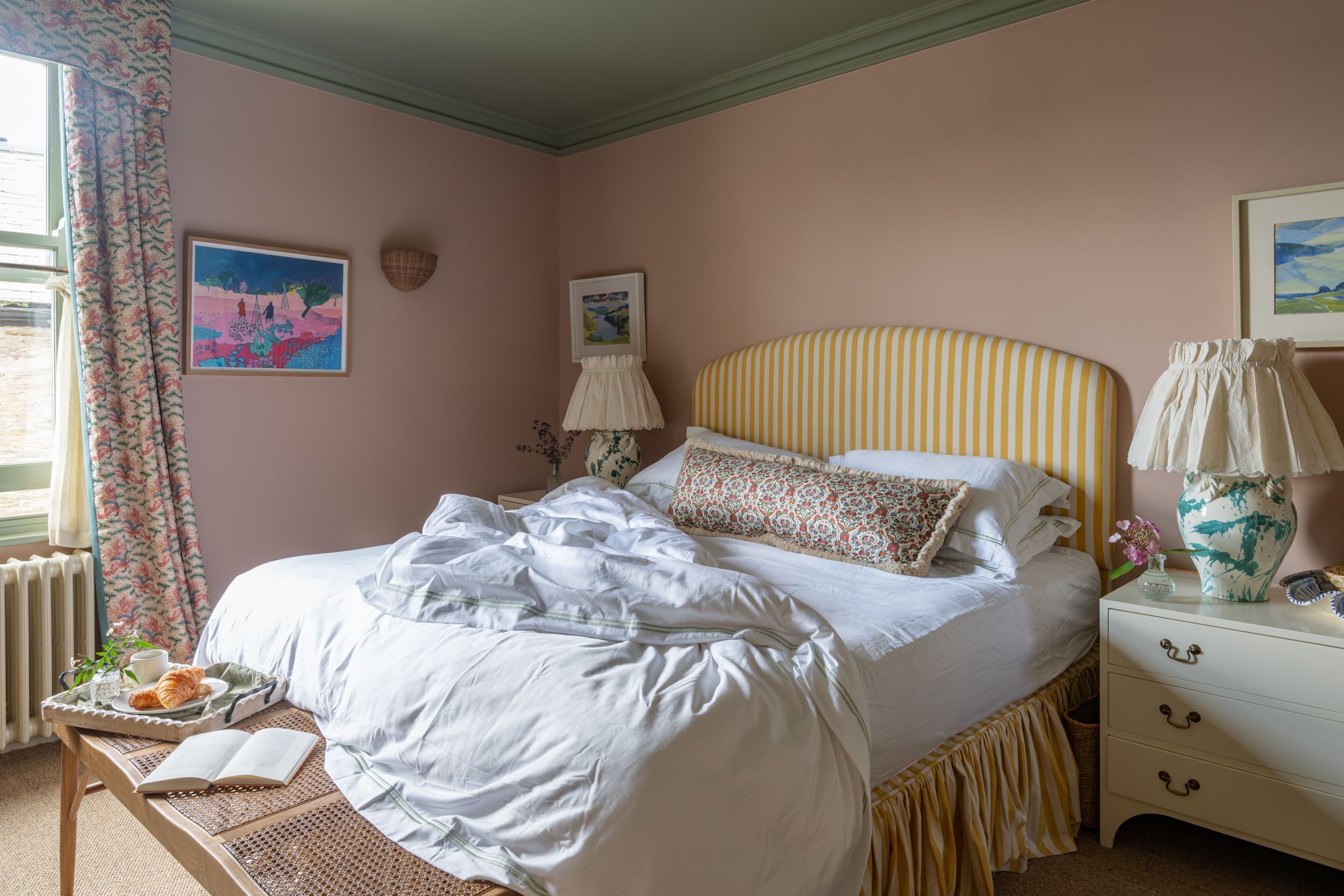 Ein ordentlich bezogenes Bett mit einem gestreiften Kopfteil, ein Nachttisch mit einer Lampe und ein gerahmtes Bild an der Wand.
