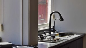 Une cuisine dotée d’un robinet moderne, d’une fenêtre avec des stores et d’un plan de travail sur lequel sont disposés divers ustensiles de cuisine.