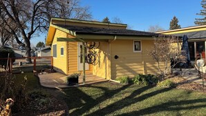 Une petite maison jaune avec un porche, un support à vélos et un petit jardin.