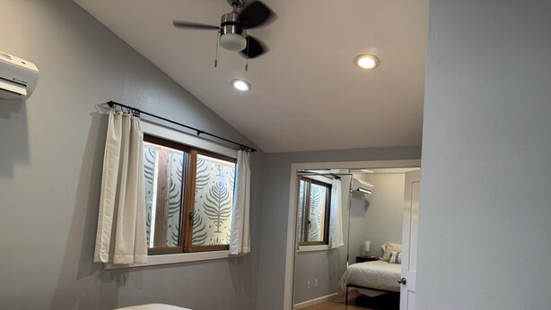 Une chambre à coucher avec un lit, un ventilateur de plafond et une fenêtre avec des rideaux.