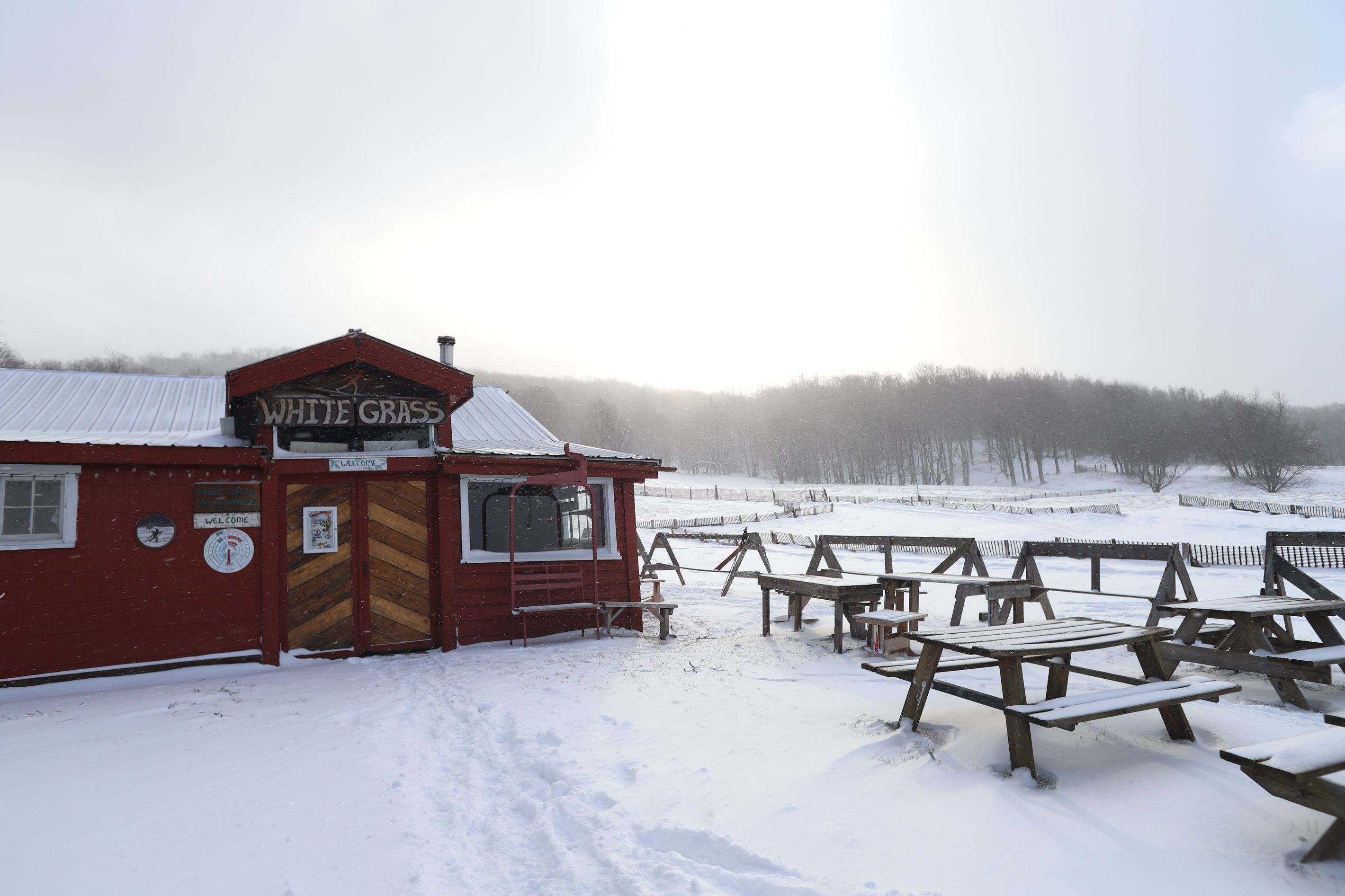 A red building with a sign reading 'WHITE GRASS' and a wooden picnic area with benches and tables.