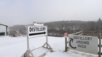 Une enseigne représentant une distillerie, recouverte de neige, avec une flèche indiquant la direction de la distillerie, et une autre enseigne précisant que la distillerie se trouve à l’arrière.