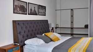 Un lit bien fait, doté d’une tête de lit capitonnée, une table de chevet avec des tiroirs et deux tableaux encadrés accrochés au mur.