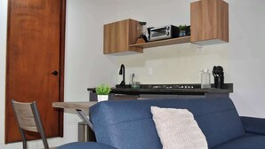 Un espace de vie compact comprenant un canapé, une table à manger, un coin cuisine équipé d’un four à micro-ondes et d’un grille-pain, ainsi qu’une porte en bois.