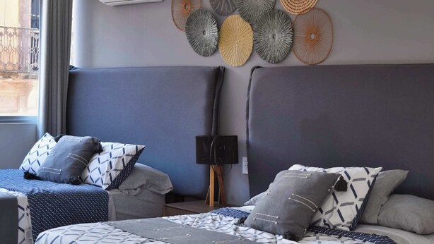 Hotellihuone, jossa on kaksi sänkyä, seinään asennettu ilmastointilaite ja koristeellinen seinävaate.