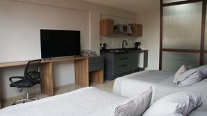 Habitació d'hotel moderna amb dos llits, escriptori amb televisió, petita cuina i finestra gran.