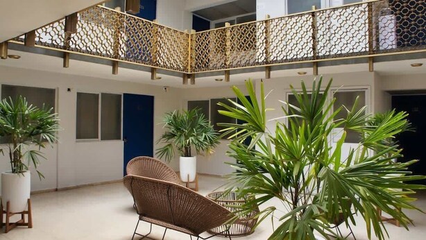 Zona interior espaiosa amb un sostre alt, una barana de fusta decorativa i diverses plantes en testos.