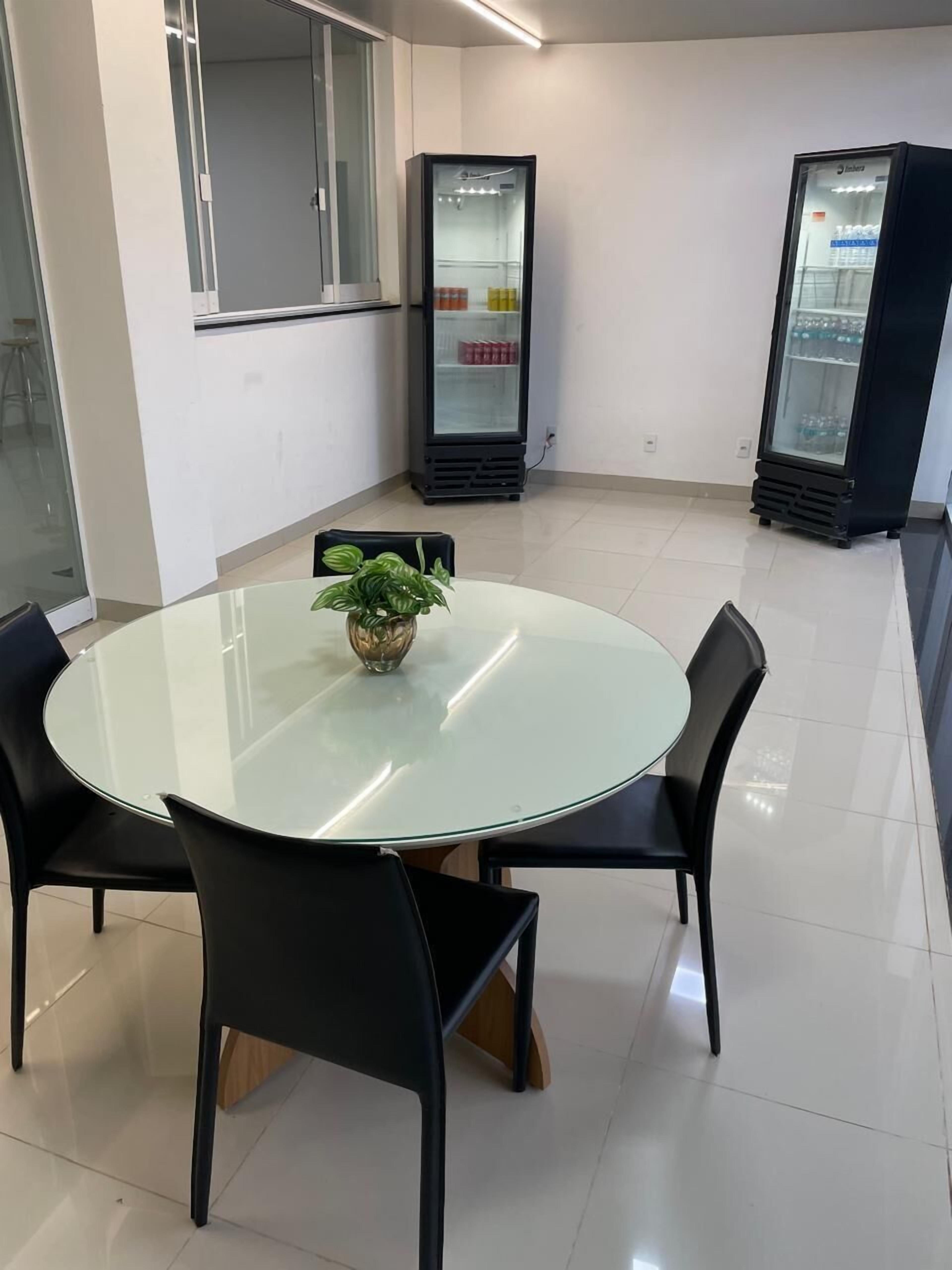 Une salle de réunion moderne avec une table en verre, des chaises noires et une plante en pot. On peut voir deux réfrigérateurs au fond de la pièce.