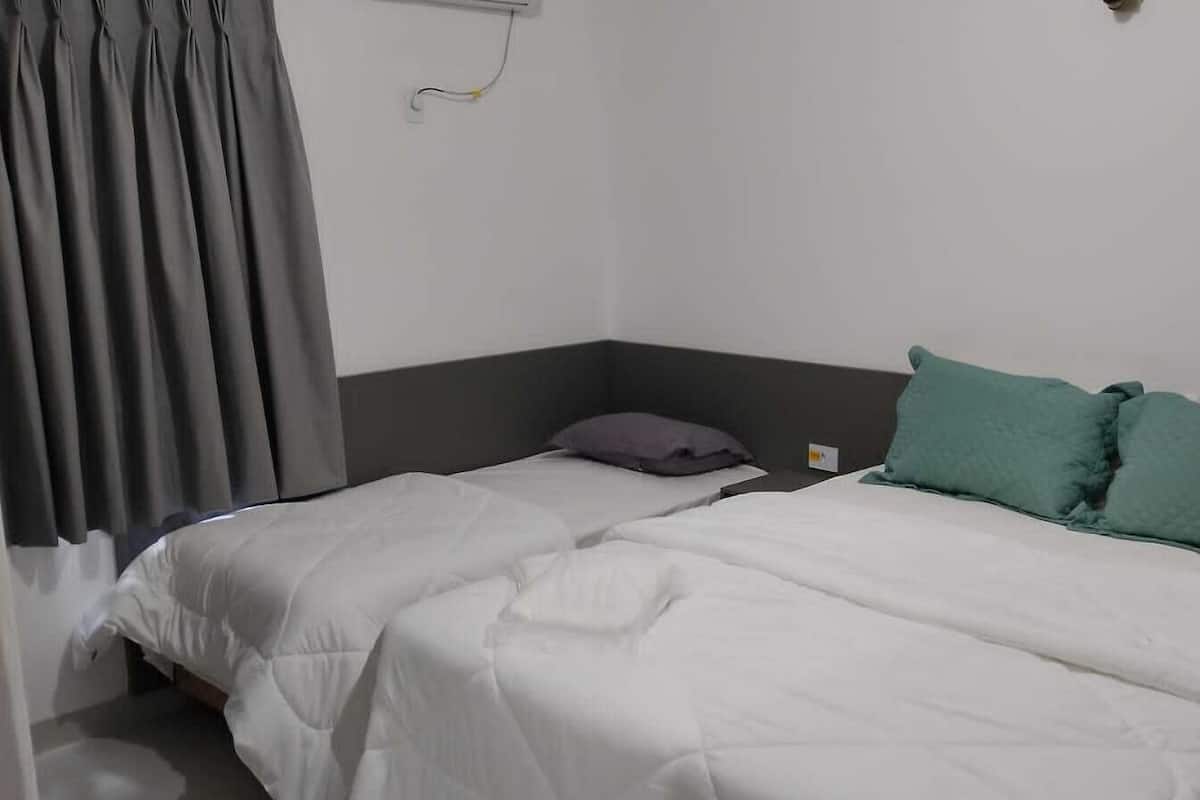 A single bed with white bedding, a grey headboard, and a teal pillow.