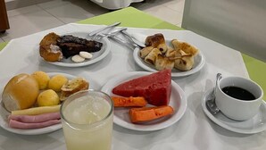 A breakfast setting with a table set for two, featuring plates of pastries, fruits, and a glass of juice.