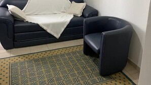 A living room with a dark blue sofa, a white throw blanket, a black armchair, and a patterned rug.