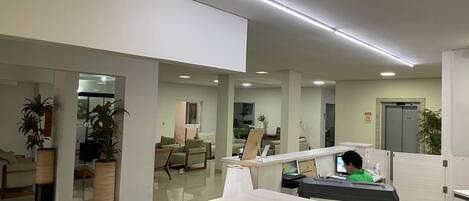 Un espacio de oficina moderno con cubículos, un mostrador de recepción y una zona de estar con sillas y un sofá.