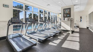 A gym with treadmills, ellipticals, and a pool view.