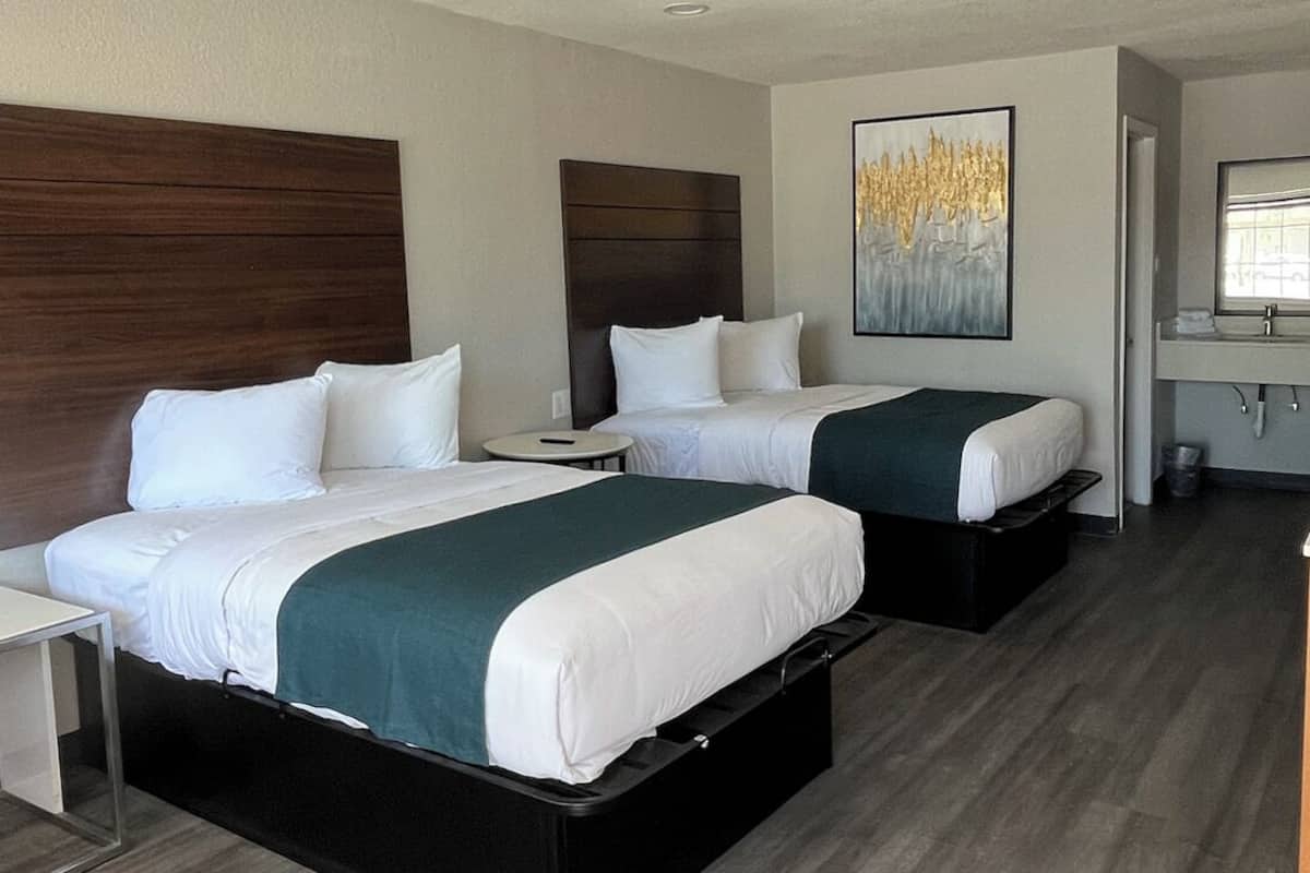 A hotel room with two beds, a small bedside table, a nightstand, a mirror, and a painting on the wall.