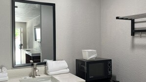 Een moderne badkamer met een wit wastafelmeubel, een grote spiegel, een zwarte magnetron en een handdoekrek.