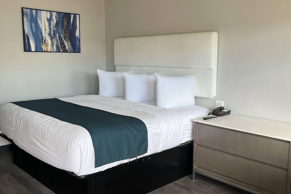 A modern hotel room with a large bed, a bedside table, and a desk.
