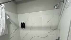 Een douche met witte marmeren wanden, een handdouche en een handdoekrek met een witte handdoek.