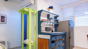 A compact kitchen with a built-in microwave, a refrigerator, and a small shelf with dishes. - Studio 4 Casiguaya (Vieques)