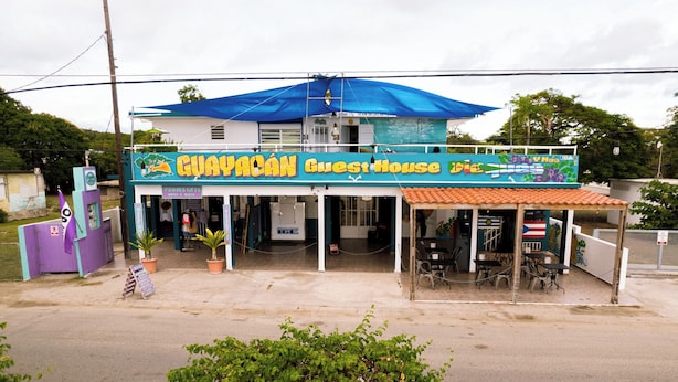 A guesthouse with a blue roof, outdoor seating, and a sign advertising "Quavascon Guest House." - Studio 4 Casiguaya (Vieques)