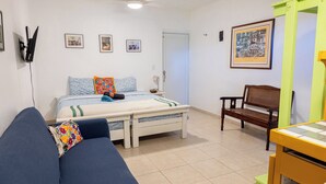 A bedroom with a bed, a blue sofa, a wooden chair, a small table, and a wall-mounted TV. - Studio 4 Casiguaya (Vieques)