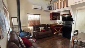 A living room with a fireplace, a sofa, a dining table, and a kitchen area with a refrigerator and microwave. - Calypso's Hideaway in delightful Pine with WiFi, AC (Pine)