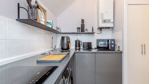 Una cocina moderna con armarios grises, una placa de inducción negra, un microondas y una tetera.