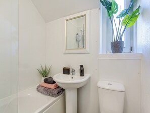 Un baño con una bañera blanca, un lavamanos pedestal, un inodoro, un espejo y una planta en maceta junto a la ventana.