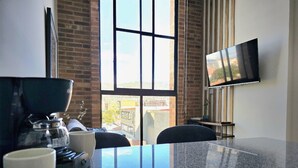 A modern kitchen with a coffee maker, a large window with a city view, and a flat-screen TV mounted on the wall. - Atelier Cedritos by Weeki. (Bogotá)