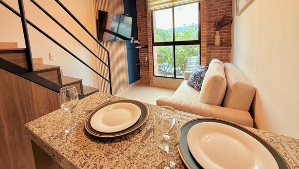A modern kitchen with granite countertops, a dining area with a sofa, and a large window with blinds. - Atelier Cedritos by Weeki. (Bogotá)