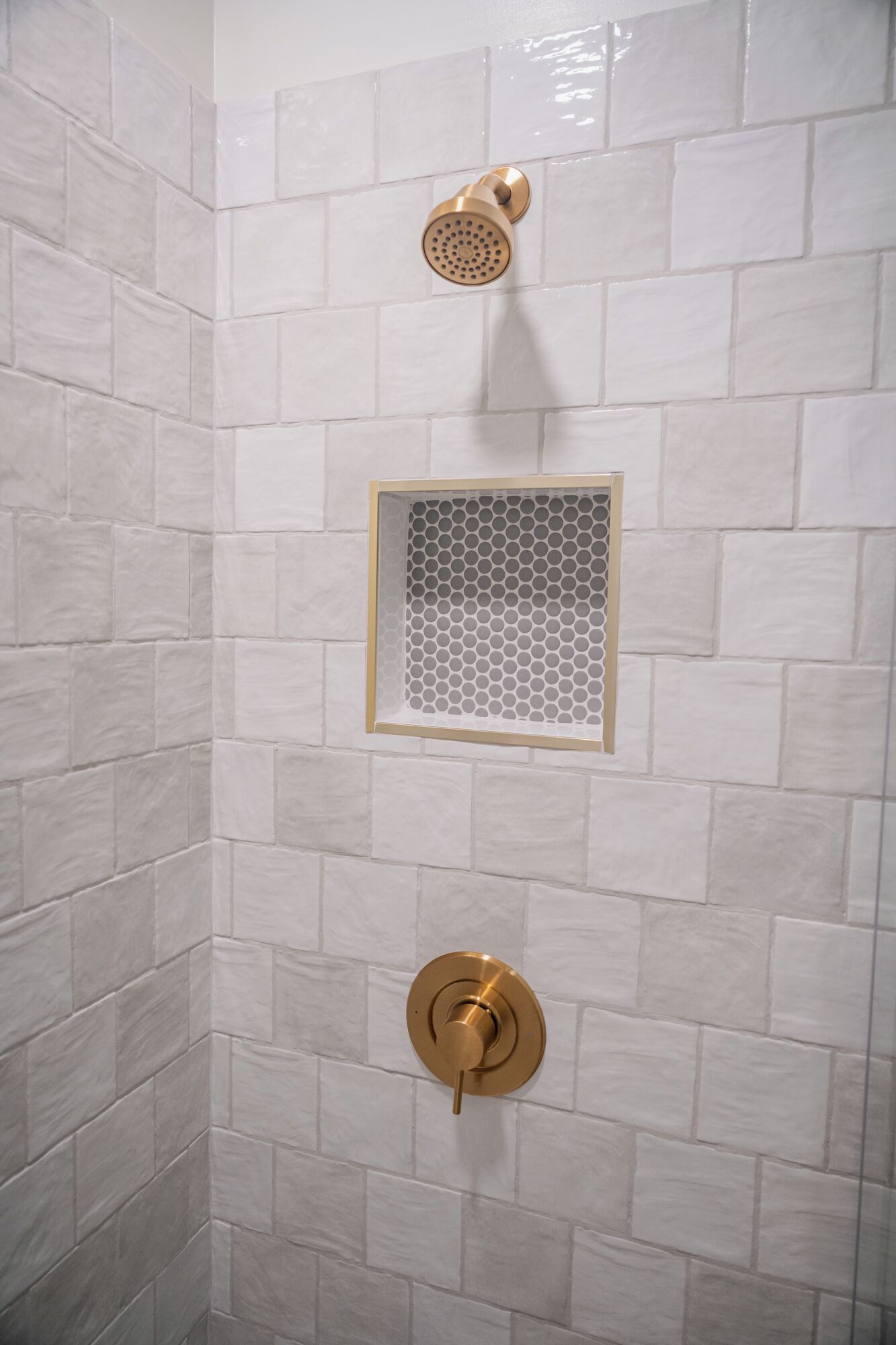 Une douche dotée d’un pommeau de douche doré et d’un robinet doré, le tout installé sur un mur recouvert de carreaux blancs.