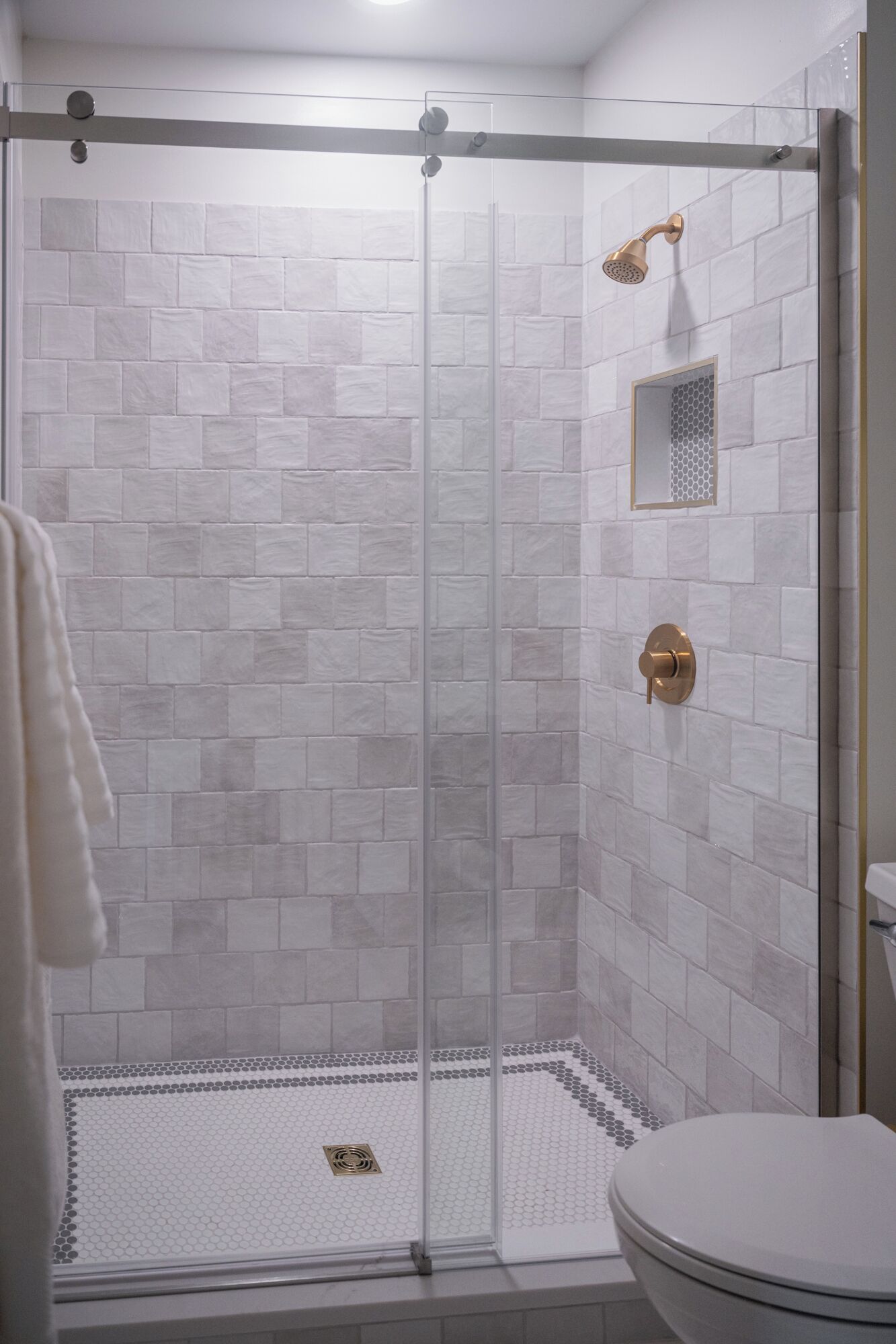 A shower area with a glass door, white tiled walls, and a toilet with a white lid.