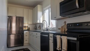 A modern kitchen with stainless steel appliances, white cabinetry, a large window, and a black countertop. - Kellys Suite (Geneva)