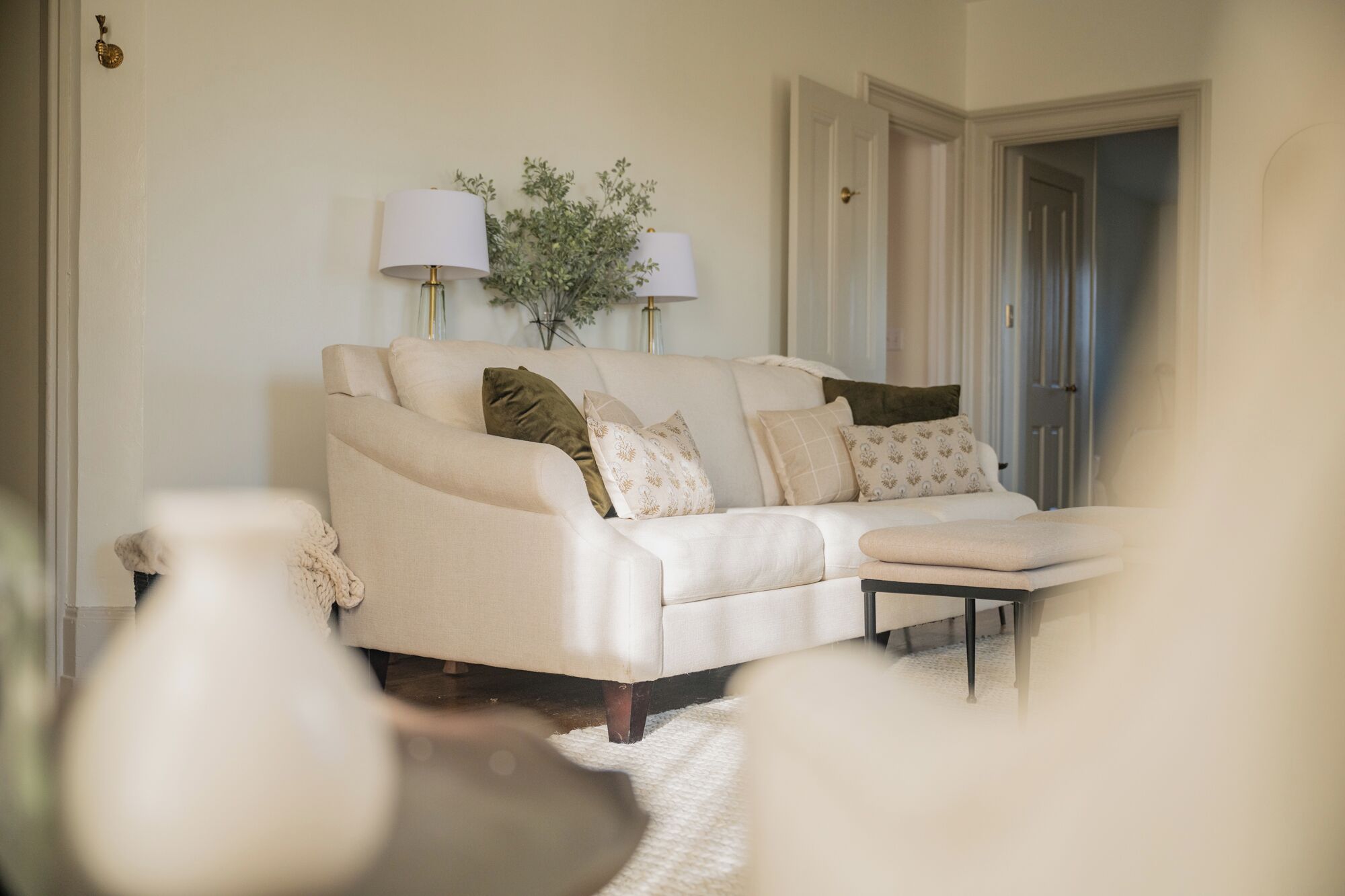 A living room with a beige sofa, multiple cushions, two lamps, and a small side table.