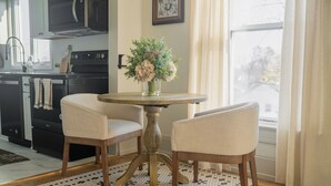 A dining area with a round table and two chairs, a vase with flowers, and a kitchen in the background. - Kellys Suite (Geneva)
