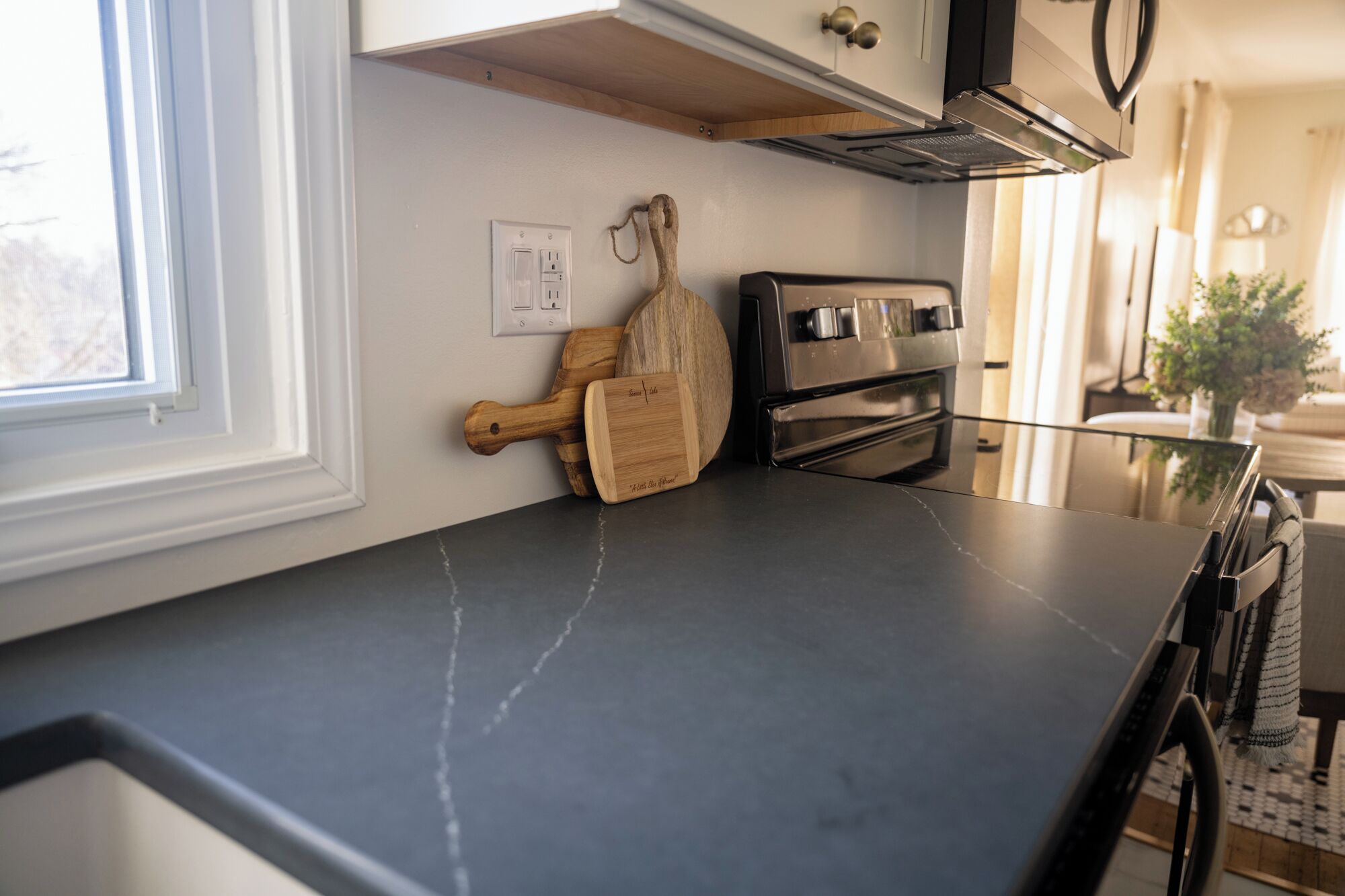 A kitchen with a black countertop, wooden cutting board, and a stainless steel oven.