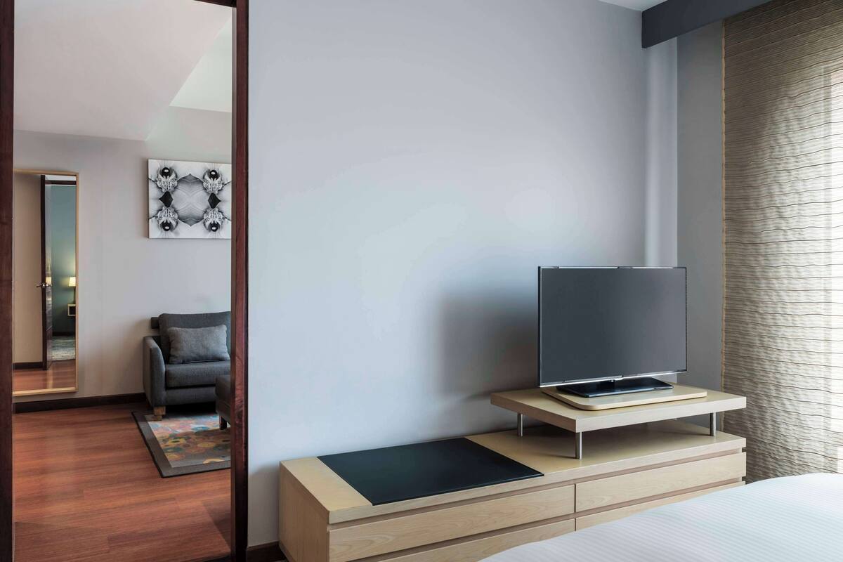 A modern hotel room with a flat-screen TV on a wooden stand, a grey sofa, and a large mirror.
