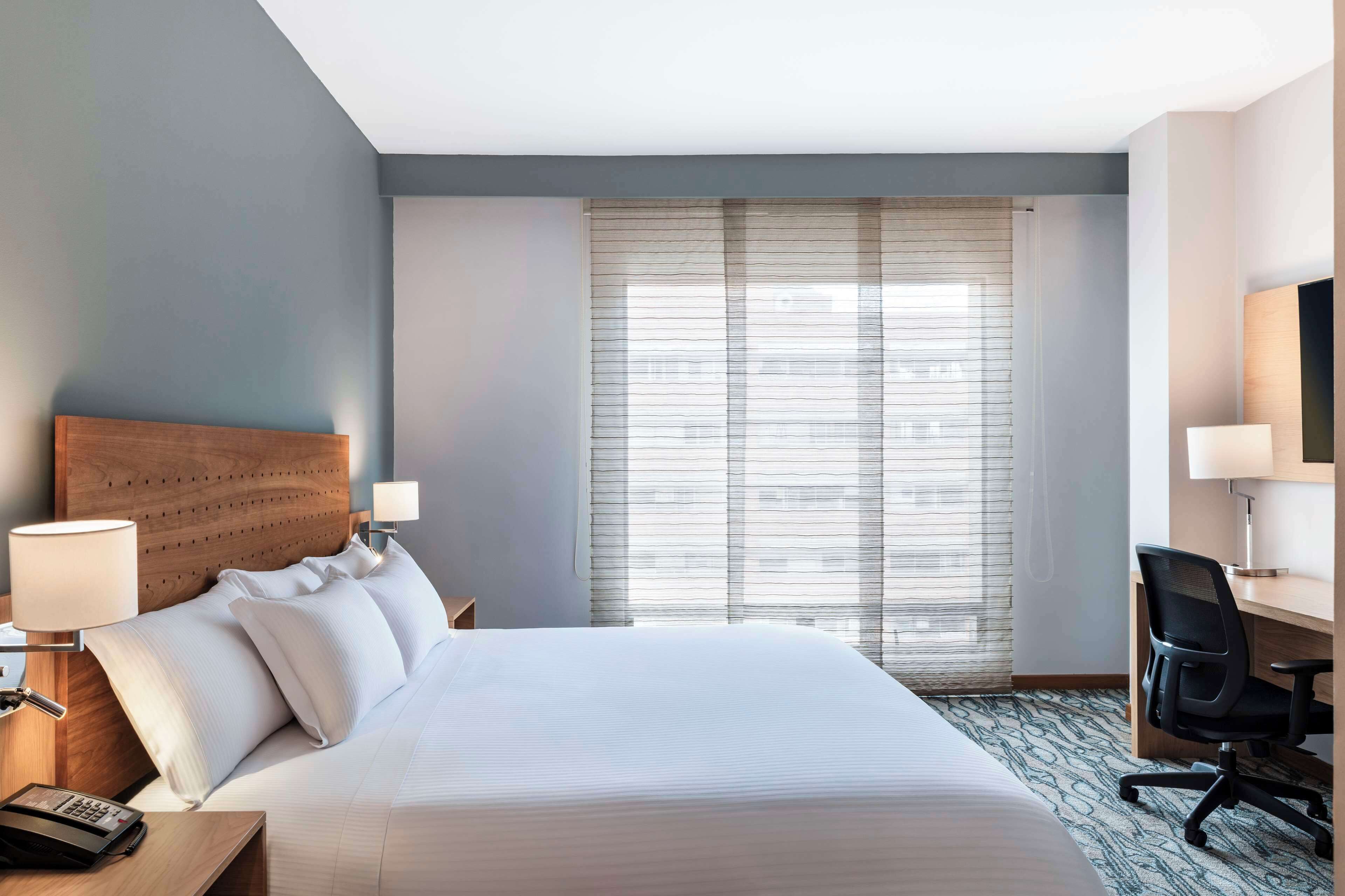 A hotel room with a large bed, a desk with a chair, a telephone, and a television.