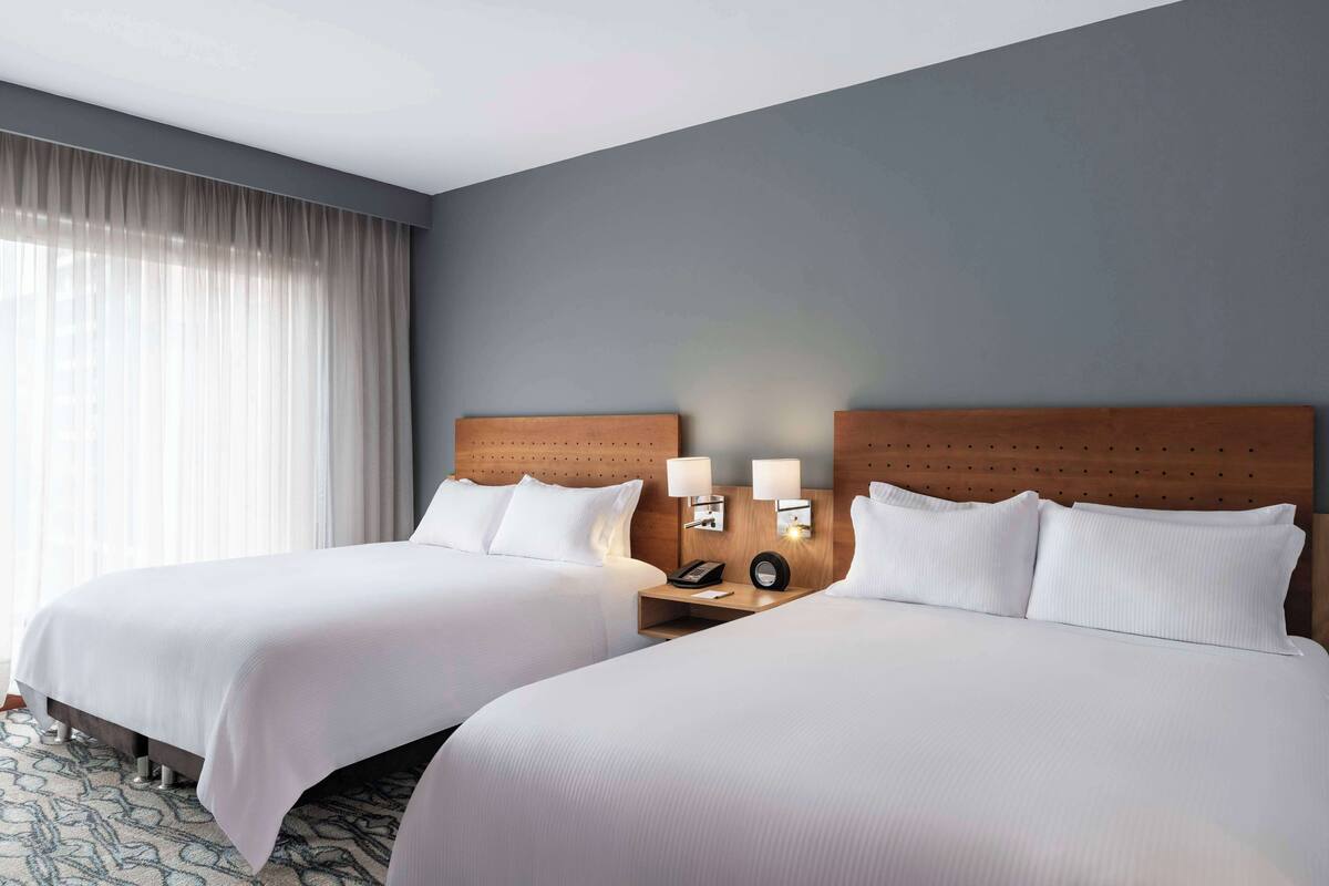 A hotel room with two beds, a wooden headboard, a nightstand with a lamp, and a telephone.