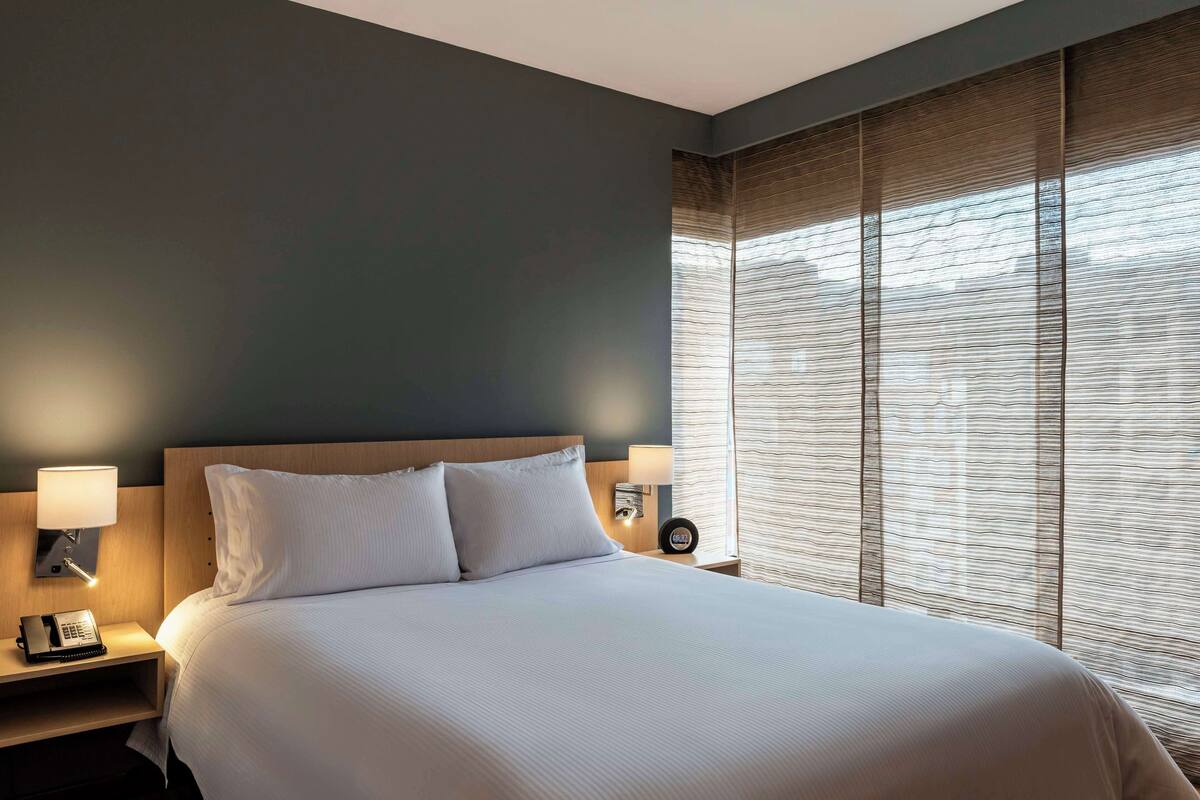 A neatly made bed with white linens, a wooden headboard, and two bedside lamps.